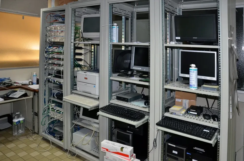 Salle technique informatique avec baies de brassage métalliques contenant équipements réseau et serveurs