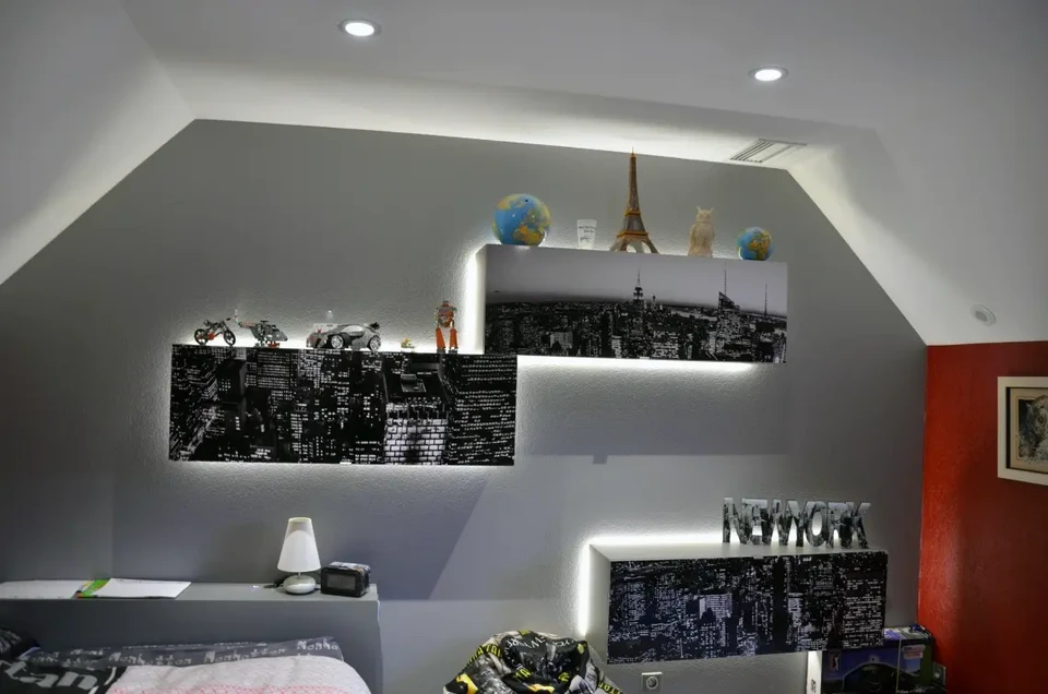 Électricien professionnel en salopette bleue et casquette installant une prise électrique murale dans une pièce blanche aux rideaux clairs